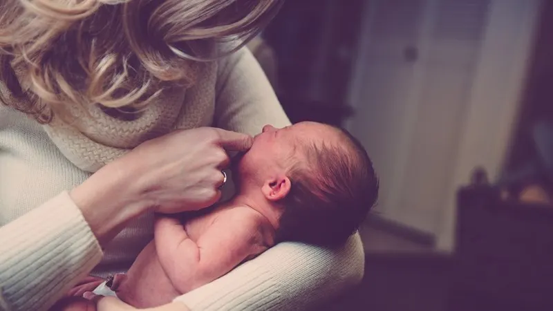 Woman holding newborn baby in indoor setting.