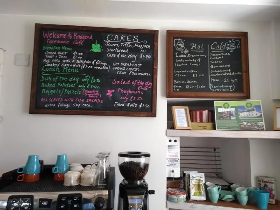 Café counter with menu boards, coffee equipment, and crockery displayed on shelves and work surface.