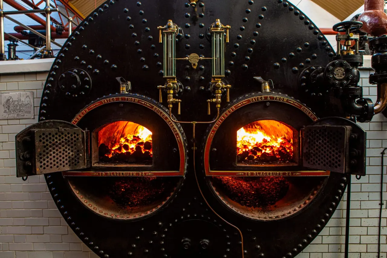 Twin cast-iron industrial furnaces with roaring fires visible through open doors, brass fittings and riveted metalwork on display.