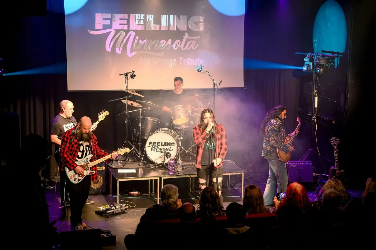 A tribute band performs on stage with guitars, drums and vocals whilst audience members watch from the front of the venue.
