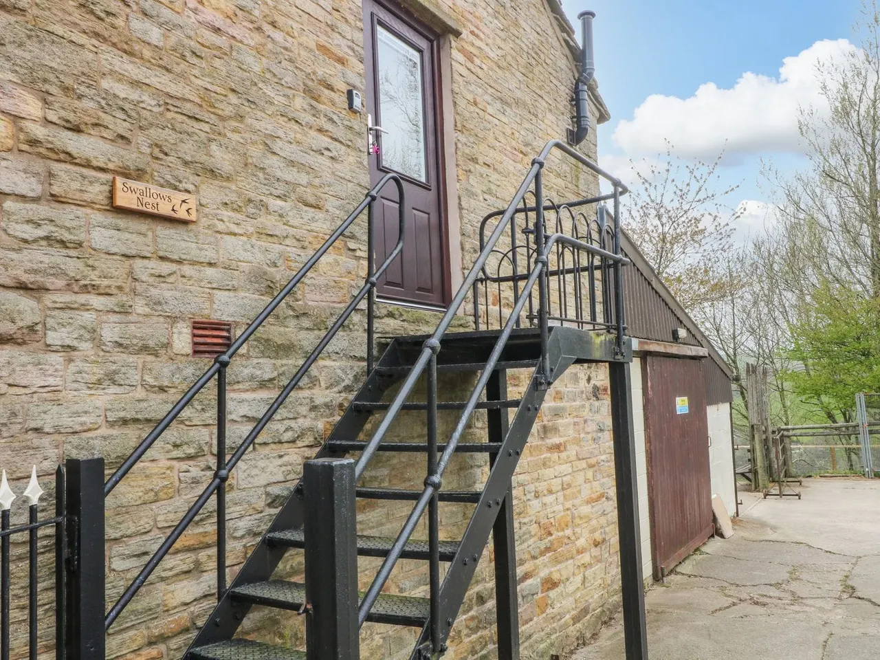 Stone farm building with metal external staircase and handrails leading to brown wooden door marked "Swallows Nest".