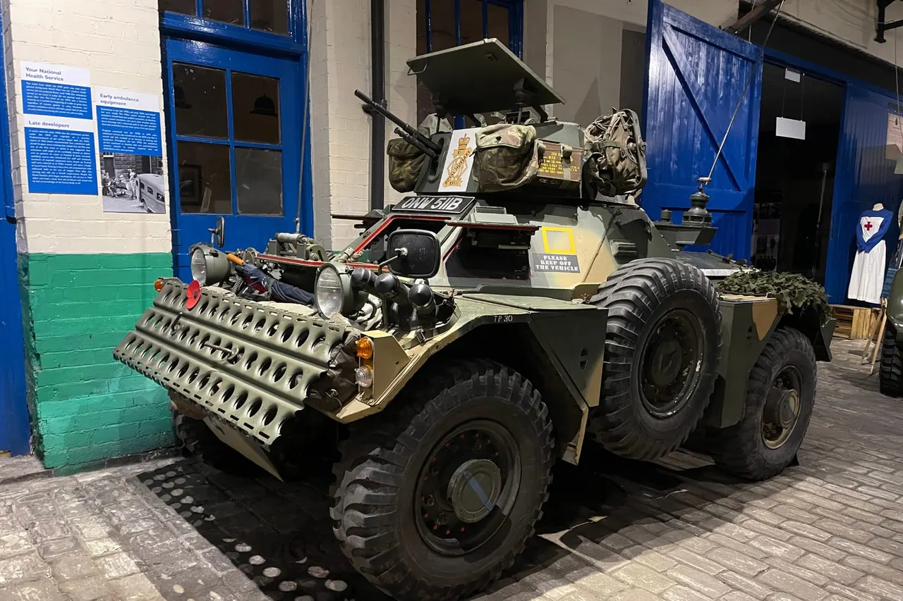 Military armoured vehicle on display in an indoor museum space with blue doors and informational panels.
