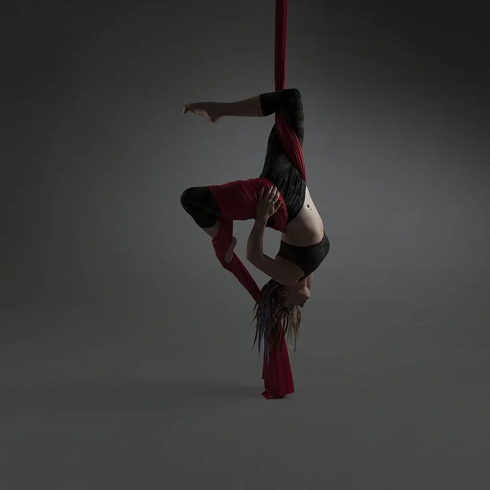 Performer suspended upside-down on aerial silk fabric during an acrobatic routine.