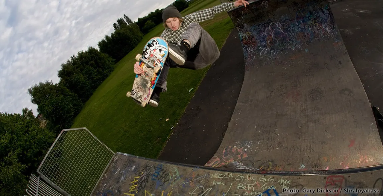 Person skateboarding on a vert ramp with green lawn and hedges visible in the background.