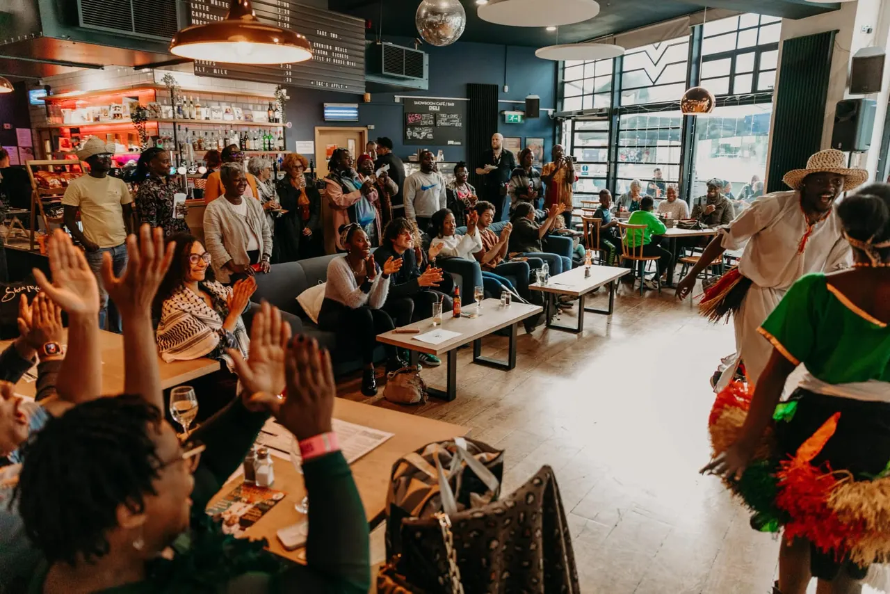 A lively café bar filled with guests clapping and enjoying a cultural performance with costumed entertainers.