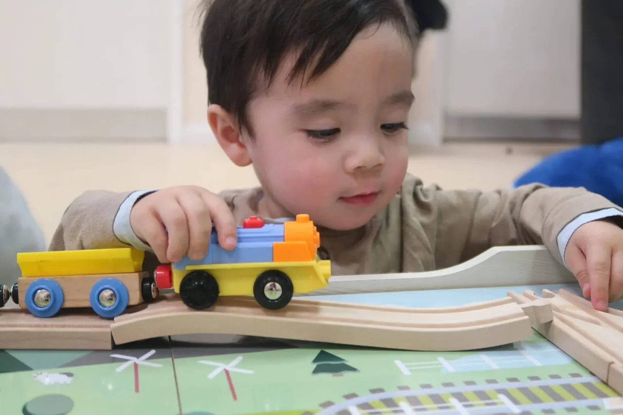Young child playing with a wooden toy train set on curved track pieces.