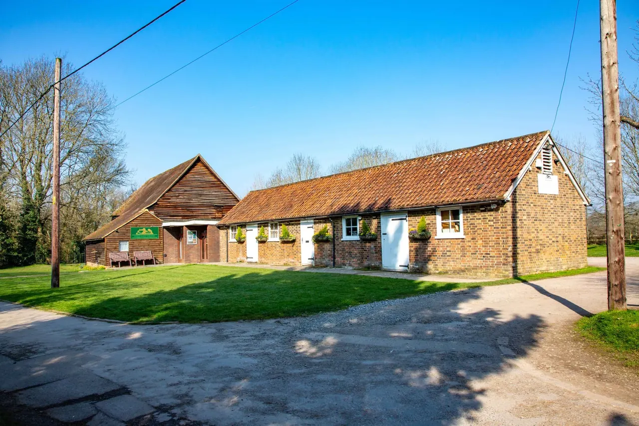 Brick buildings with tiled roofs set in rural grounds under clear blue sky, with a gravel drive and grass lawns.