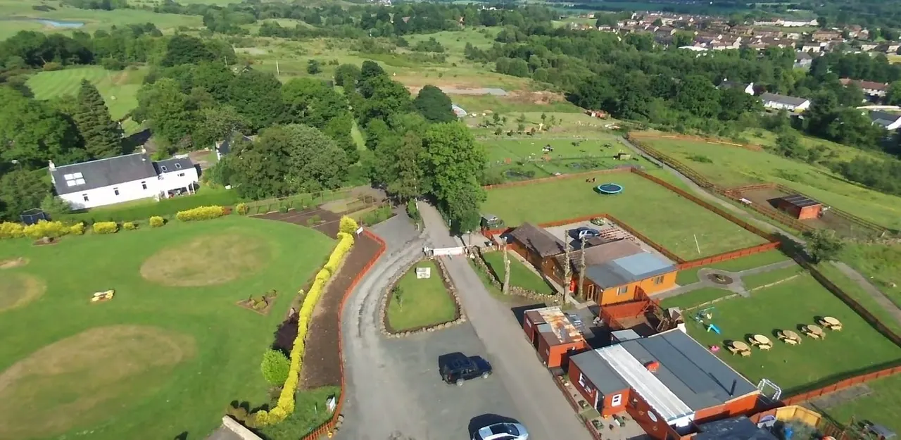 Aerial view of a rural leisure venue with paddocks, farm buildings, a white house, manicured grounds and surrounding countryside.