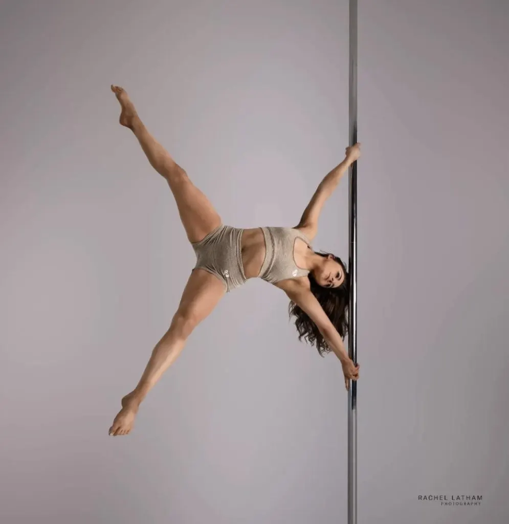 Woman performing a pole dancing move against a vertical pole with legs extended.