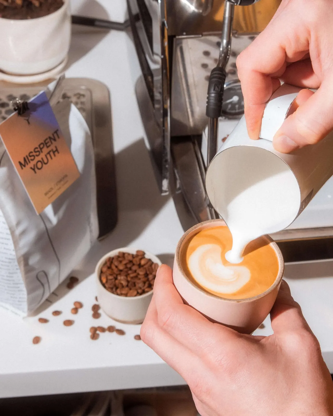 Barista pouring steamed milk into espresso to create latte art in a white cup.