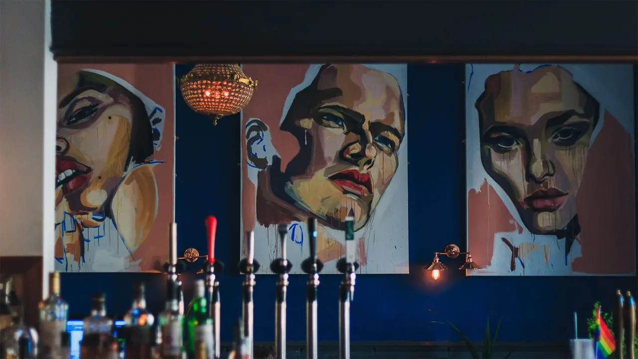 Bar interior with pop art style portrait murals on wall above beer taps and bottles.