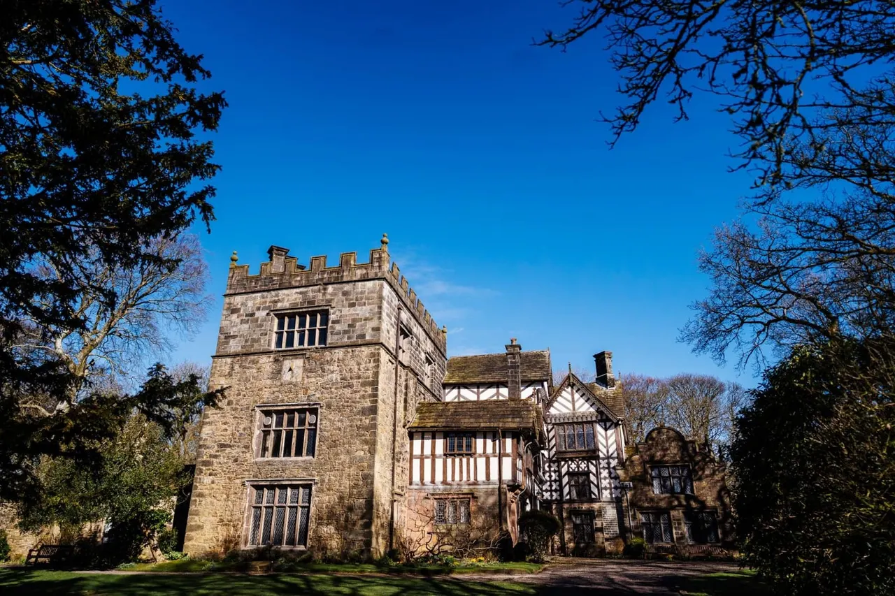 Historic stone tower and timber-framed manor house set in grounds with bare trees against a clear blue sky.