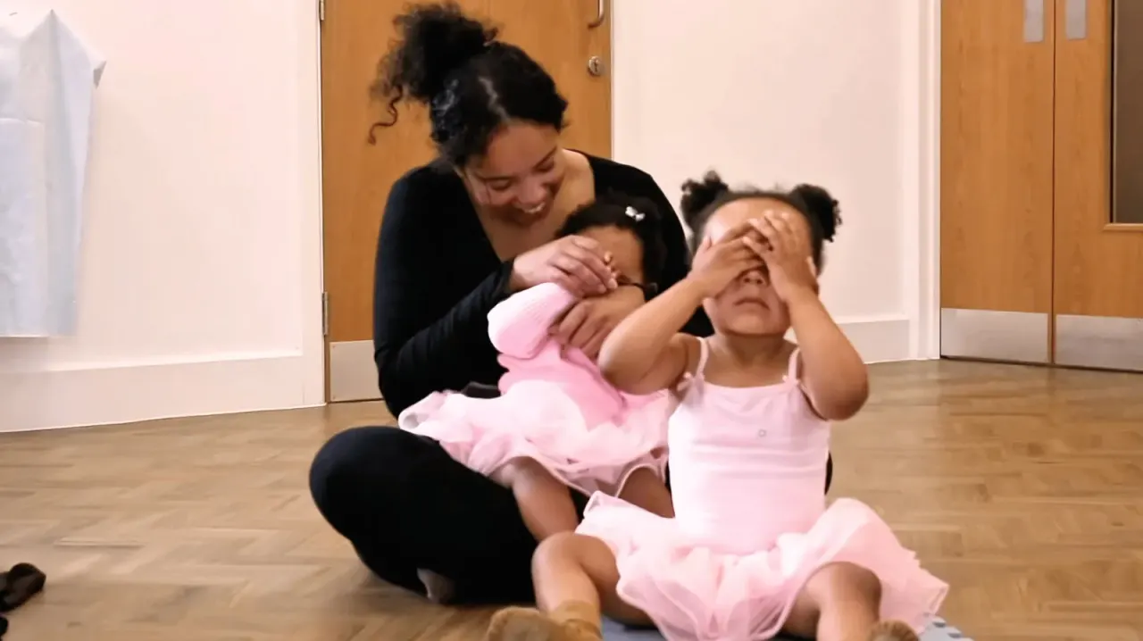 Instructor with toddlers in a babyballet studio class on parquet floor