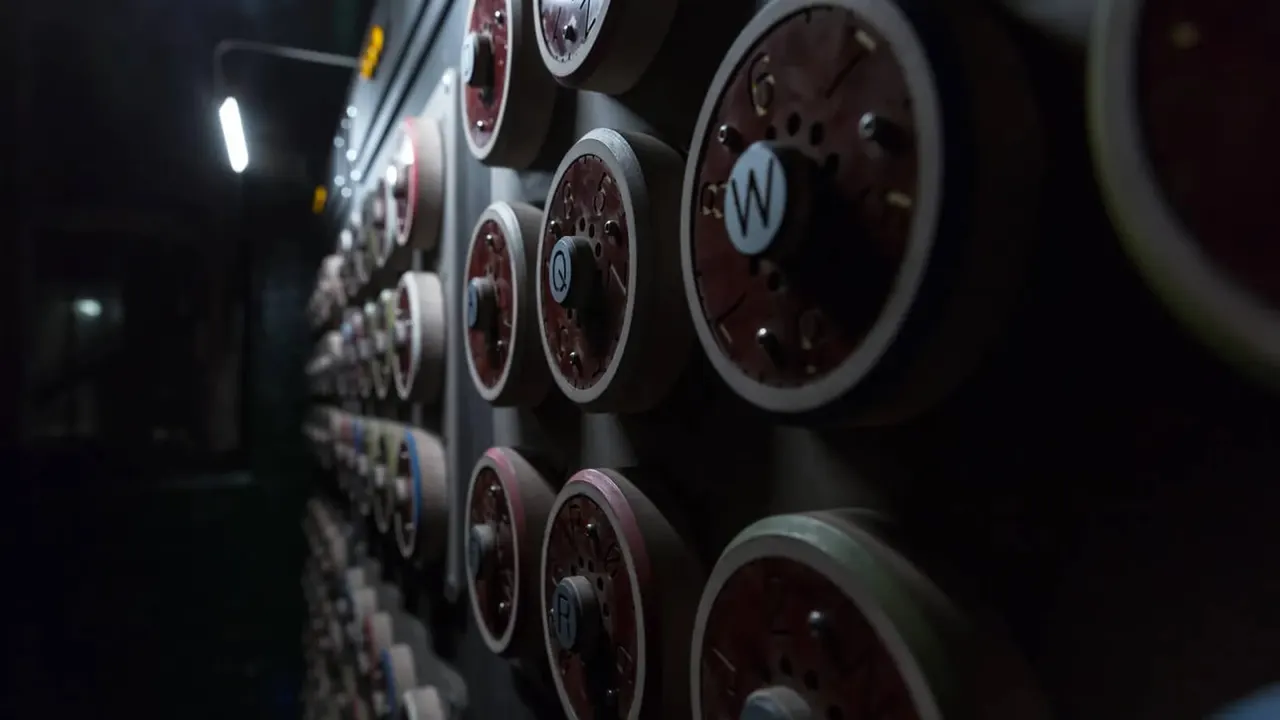 Close-up of multiple illuminated red and silver gauge dials mounted on a dark wall in an industrial setting.