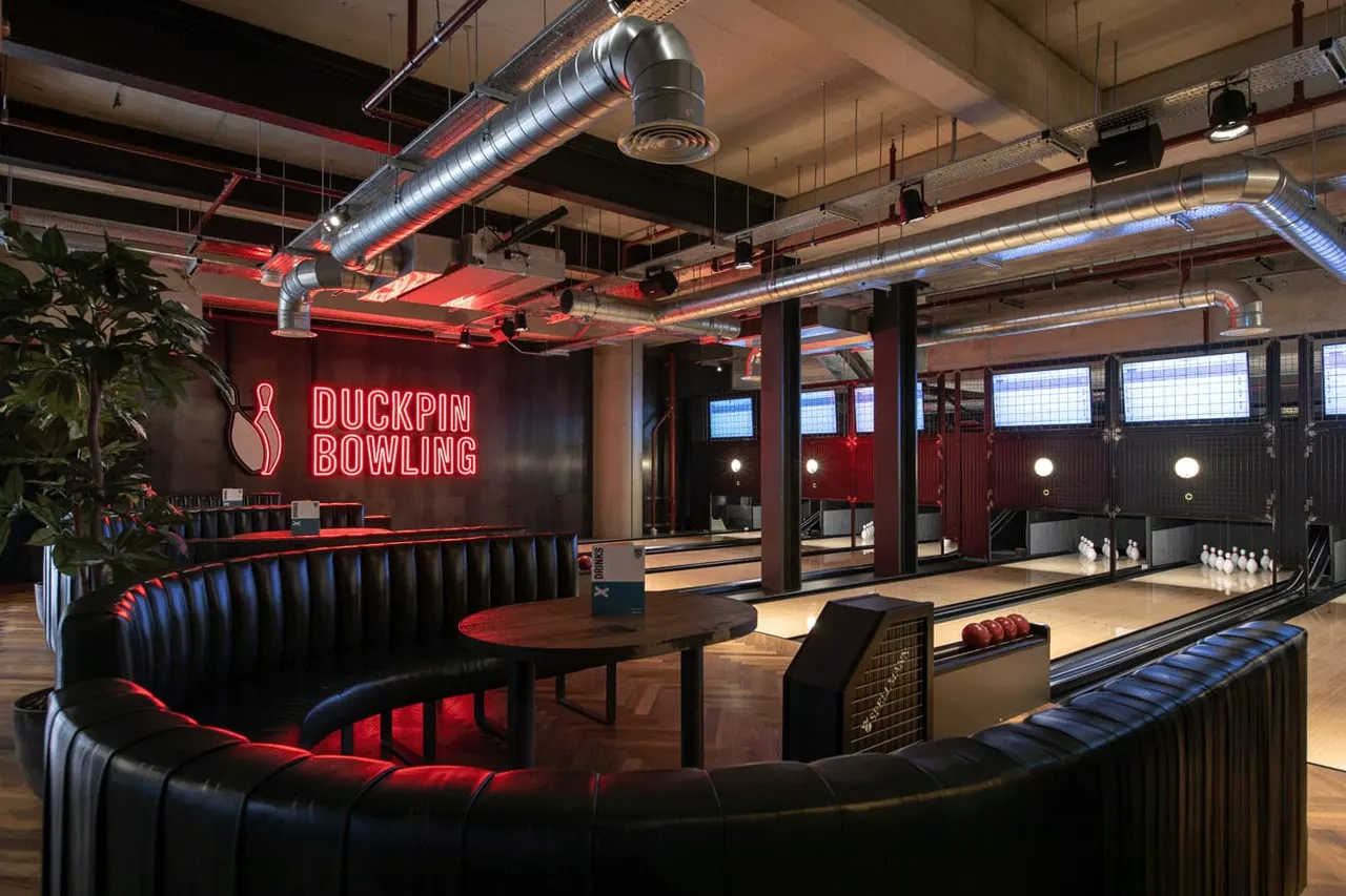 Modern bowling alley interior with neon signage, seating areas, and multiple lanes lit in red and blue.