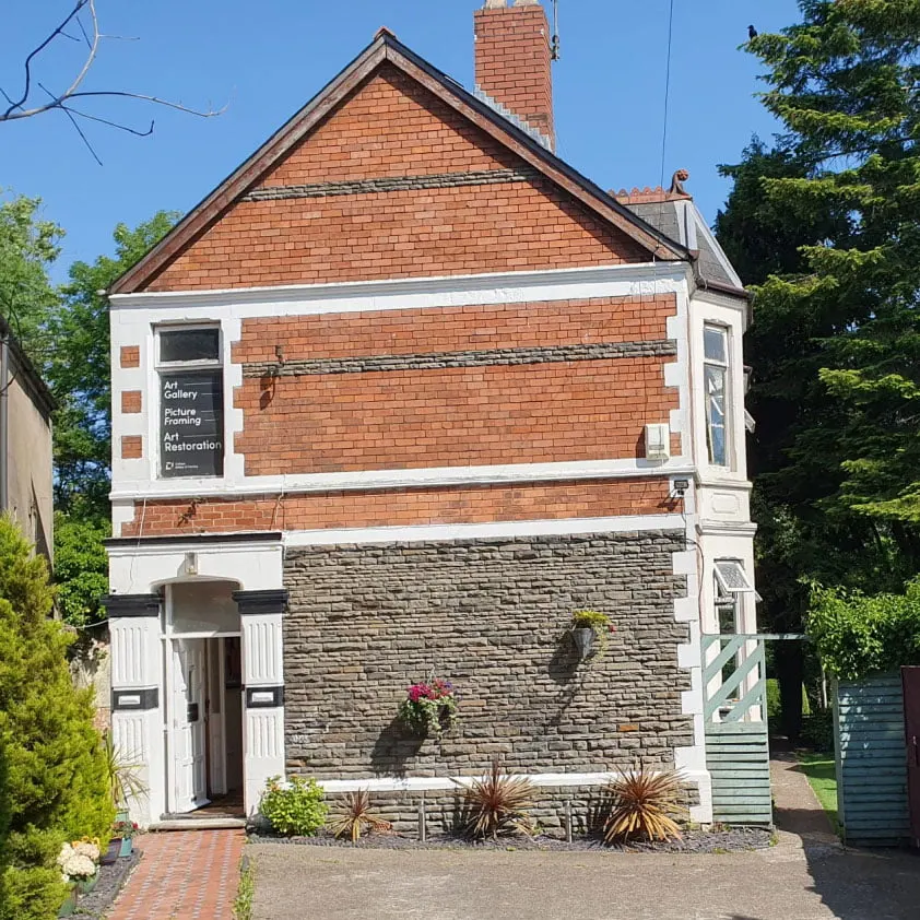 Victorian brick building with white trim housing an art gallery and picture framing shop, surrounded by greenery.