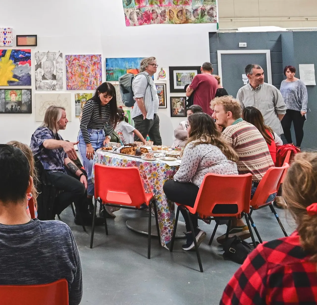 People seated around a table with food at an art gallery event, with artwork displayed on walls behind them.