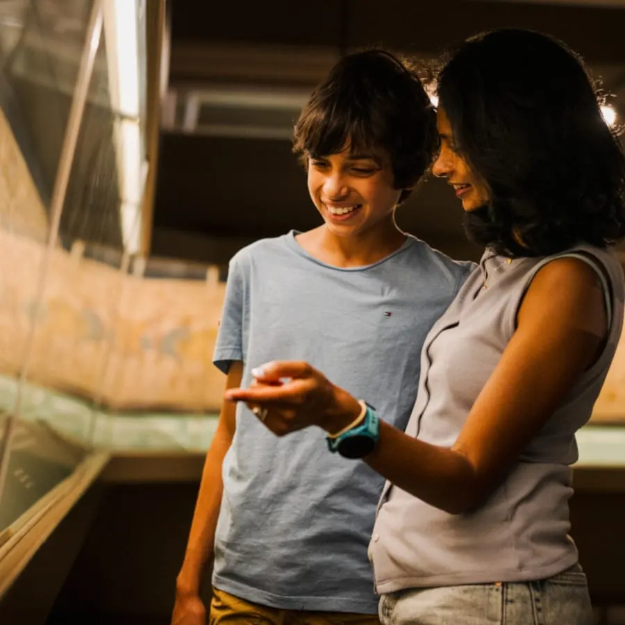 Two visitors smiling while holding and examining a small object in a museum display area.