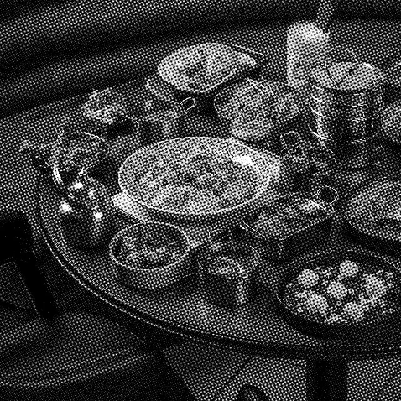 Multiple dishes of Indian curry and rice served on a round table in black and white.