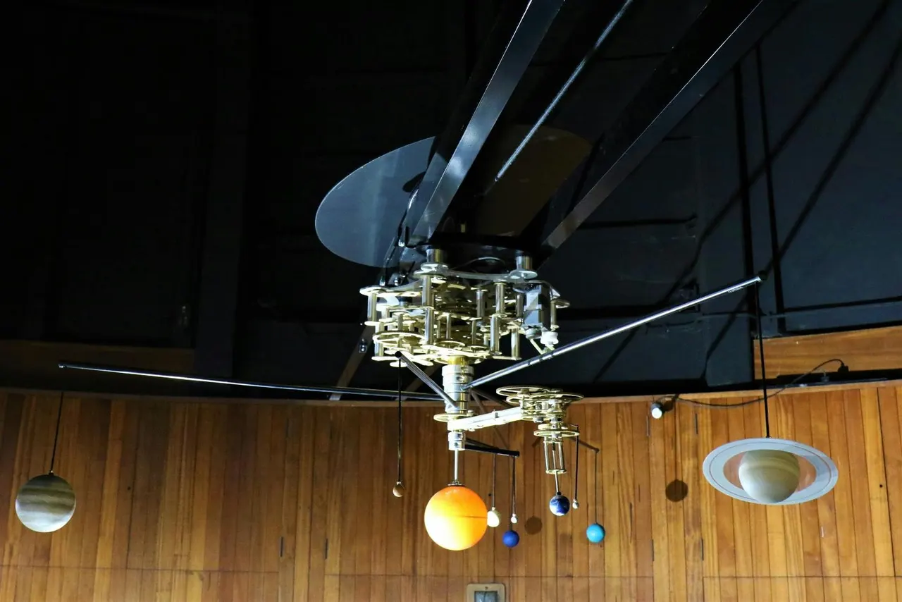 Mobile orrery and planetarium projector suspended from wooden ceiling with planets and orbital models.
