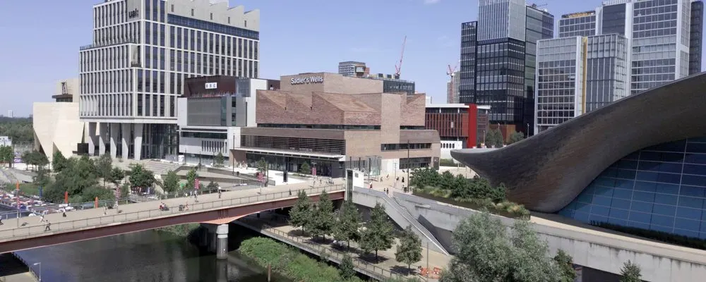 Urban waterfront with bridges, modern buildings, and a theatre complex beside a canal.