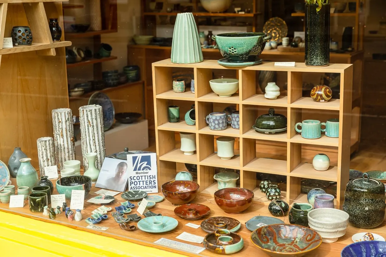 A pottery shop display with handcrafted ceramic bowls, vessels, and decorative pieces arranged on wooden shelves and a counter.