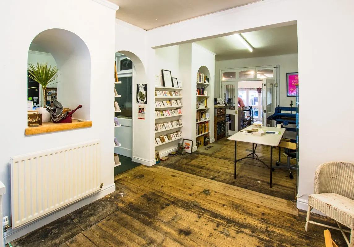 Interior of a bookshop or library with wooden floors, bookshelves, a table, and seating areas.