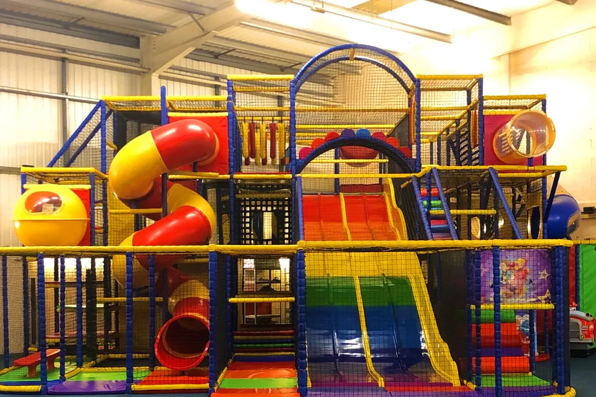 Indoor play structure with multiple levels, slides, climbing areas and tunnels in bright primary colours.