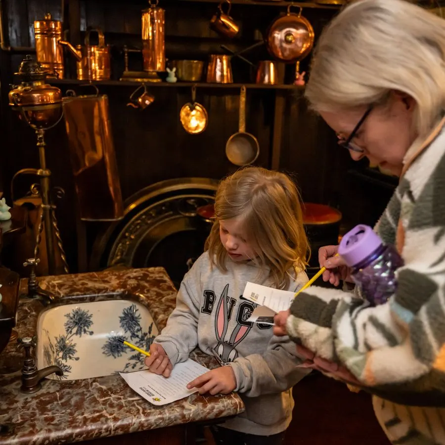 An adult and child interact at a kitchen display with copper pots and period cookware hung on the wall behind them.