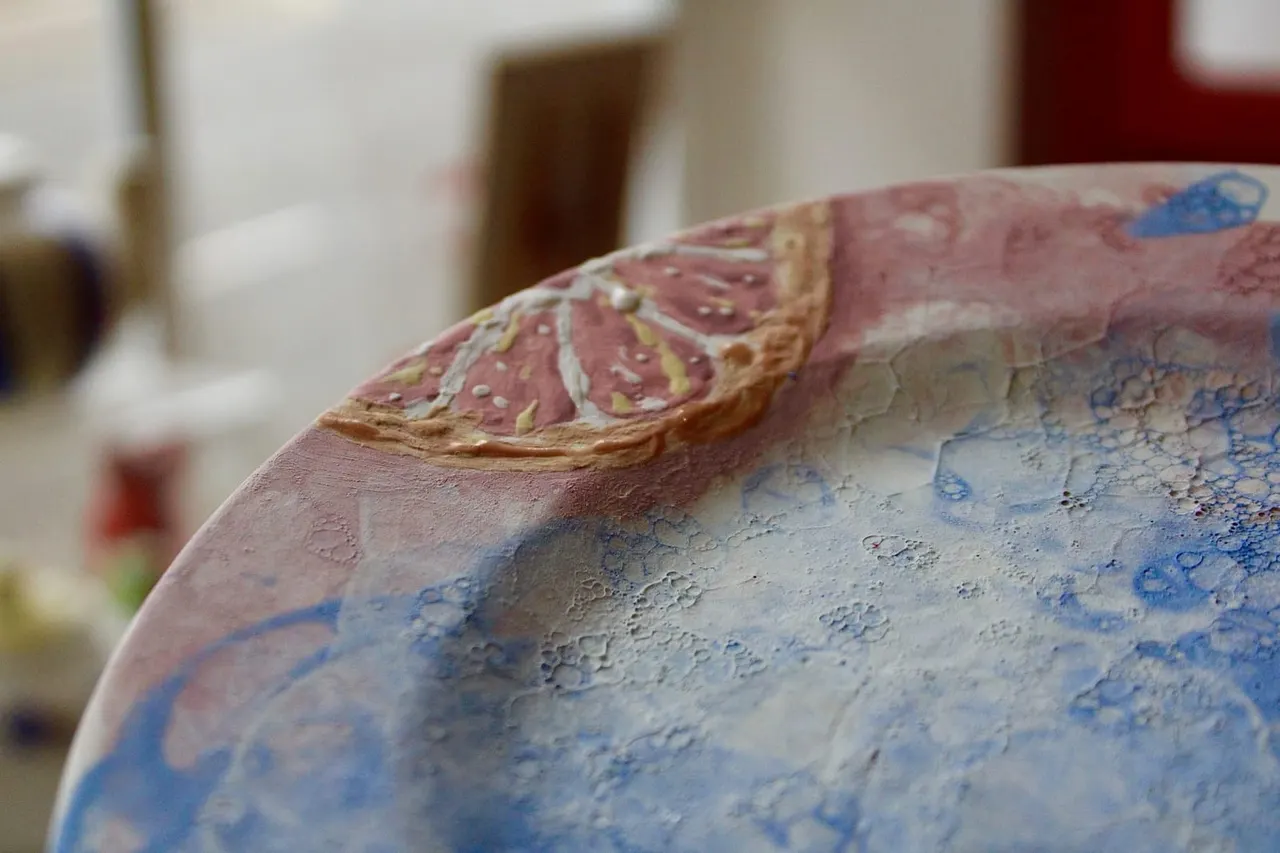 Close-up of a hand-painted ceramic bowl with pink and blue decorative patterns and gold details.