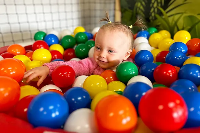 Young child smiling in a ball pit filled with colourful plastic balls.