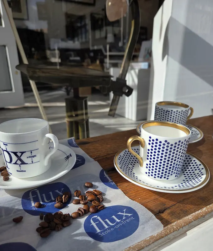 Two patterned coffee cups and saucers with roasted coffee beans on a wooden table indoors.