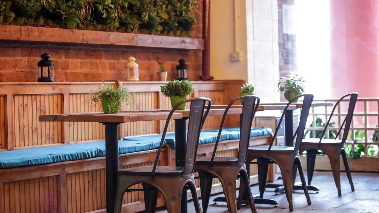 Indoor seating area with wooden table, metal chairs and blue cushioned bench against terracotta brick wall with potted plants.