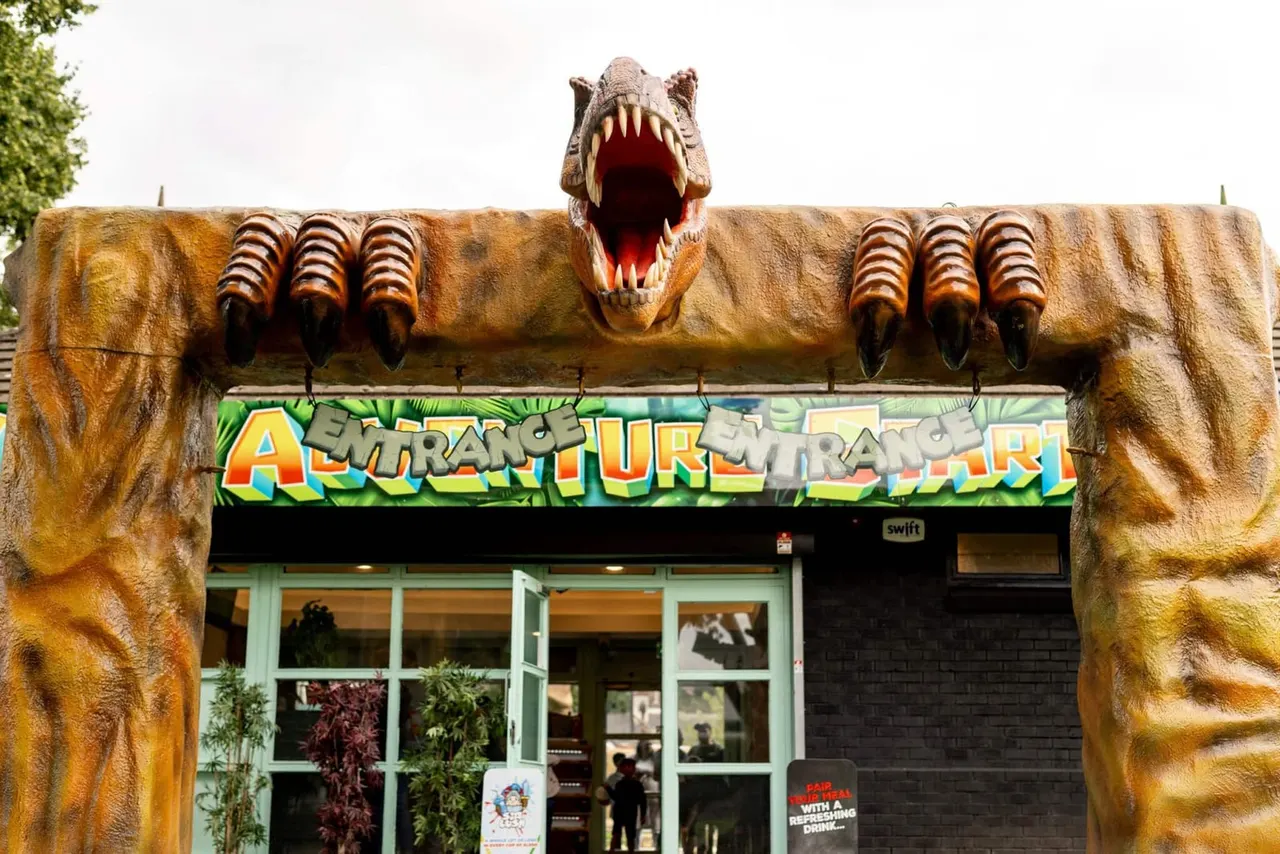 Giant dinosaur head sculpture with open jaws frames the entrance to an adventure golf attraction.