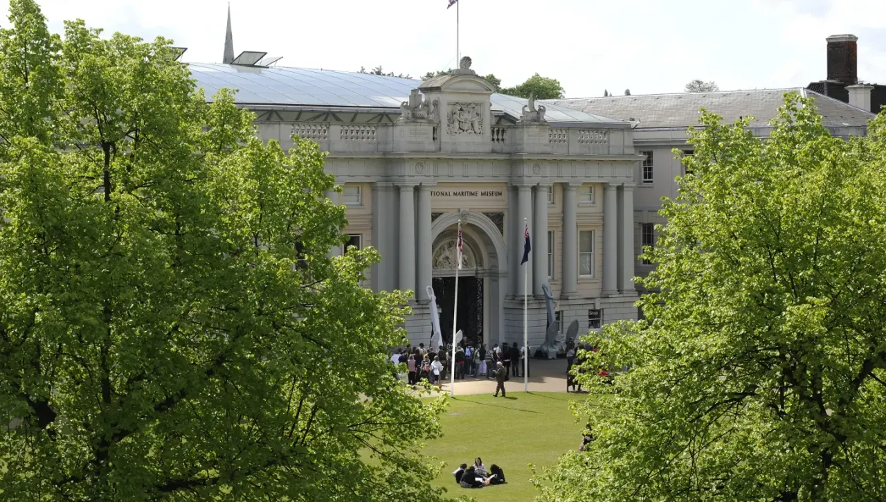 Classical stone museum building with columned entrance viewed across green lawn framed by spring foliage, visitors on grounds.