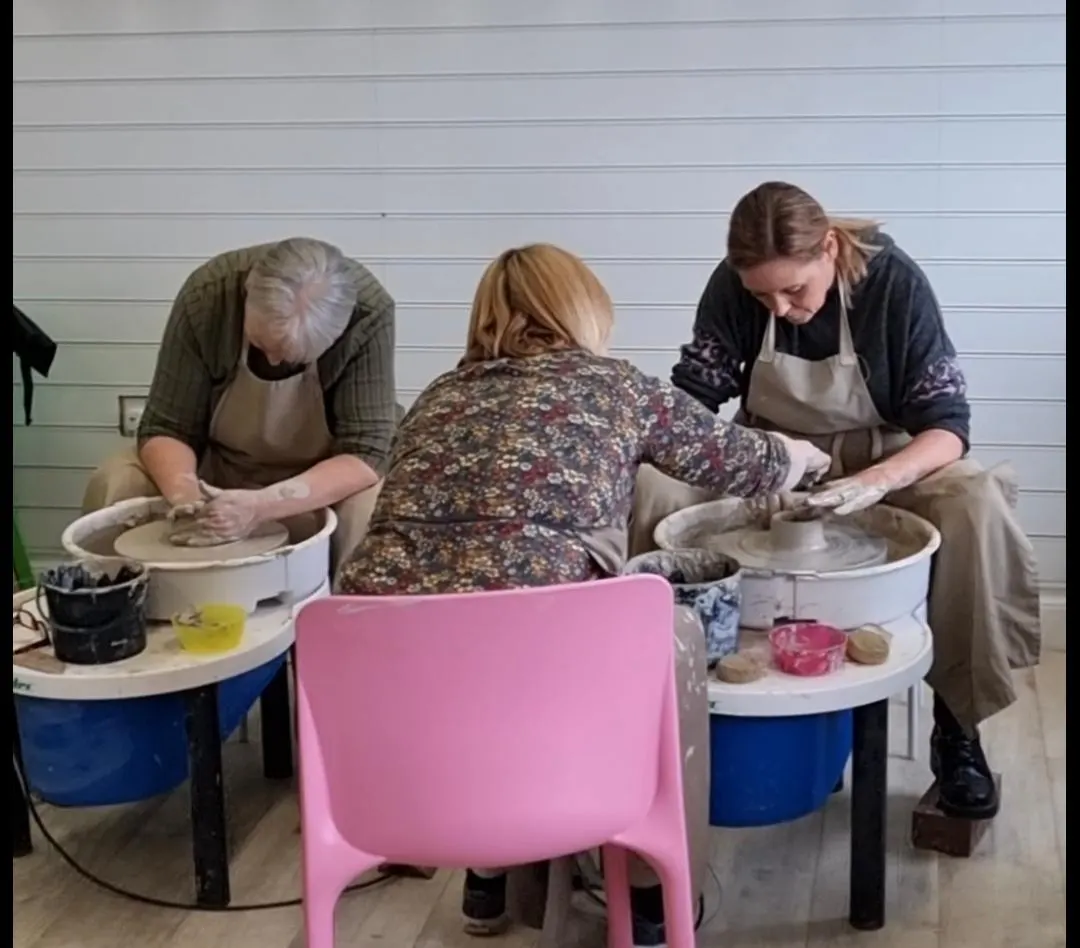 Three people working at pottery wheels, creating clay vessels during a hands-on pottery workshop.