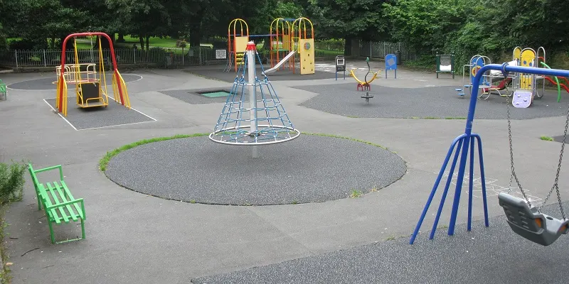 Children's playground with multiple climbing frames, slides, swings and a rope climbing dome on rubberised surfacing.