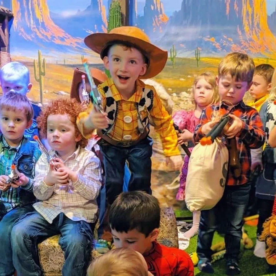 Young children in cowboy costumes posing with a character dressed as a cowboy against a desert backdrop.