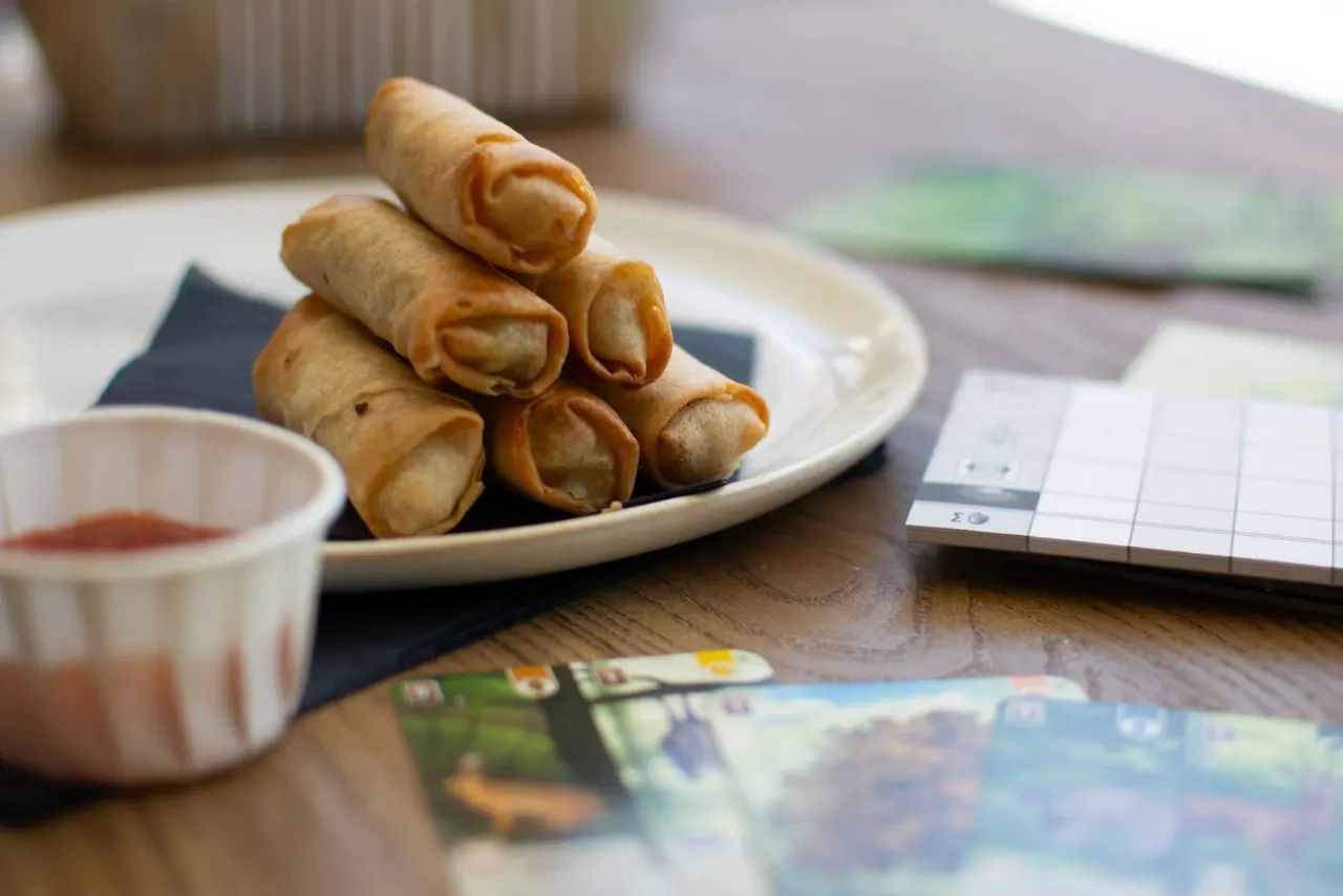 Stacked spring rolls on a plate with dipping sauce and menu cards on a wooden table.