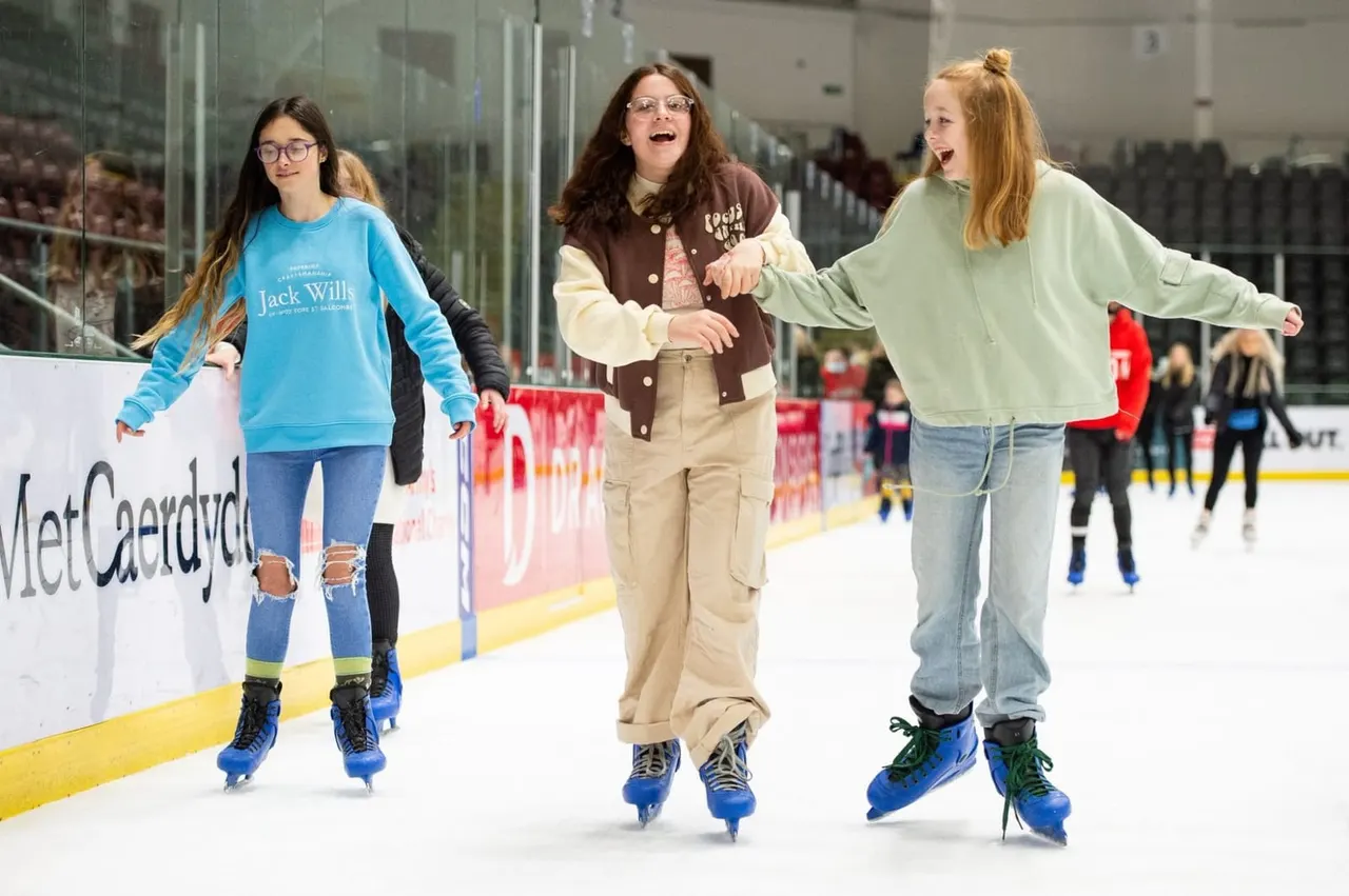 Three young people ice skating together on an indoor rink, smiling and enjoying themselves.