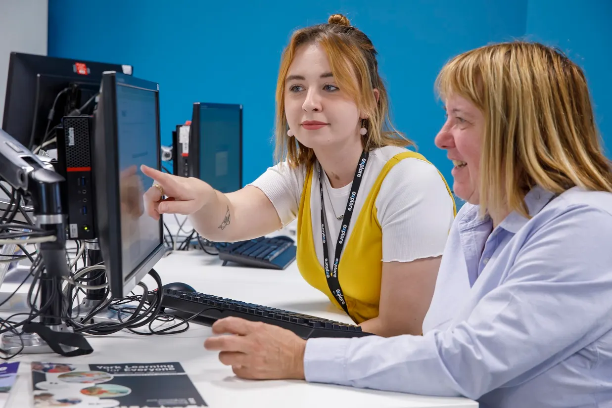 This is a GRAPHIC.

Actually, reviewing again: this is a photograph showing a young woman wearing a yellow lanyard speaking to an older woman at a computer workstation.