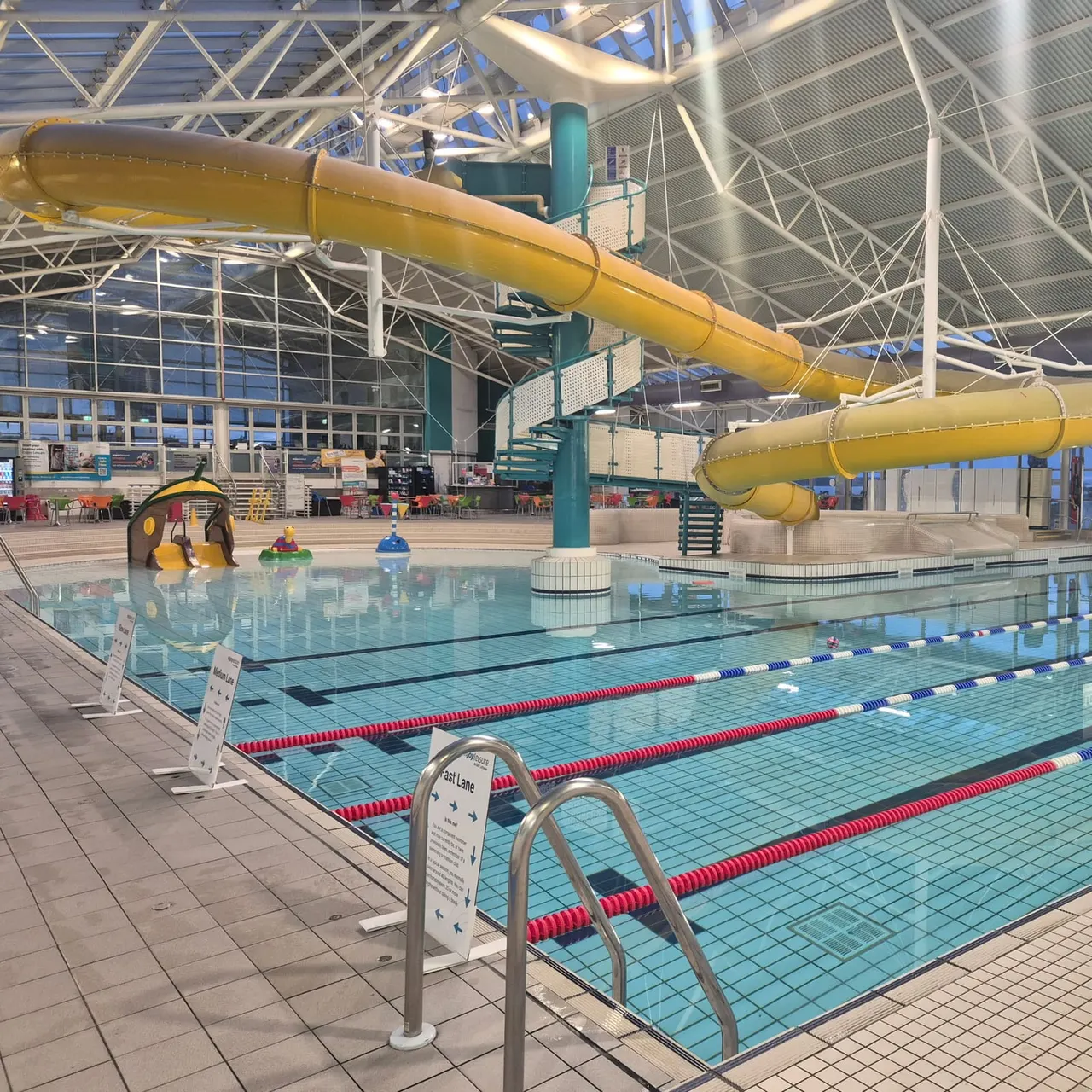 Indoor swimming pool with lane dividers, yellow water slides, and shallow play area with inflatables.