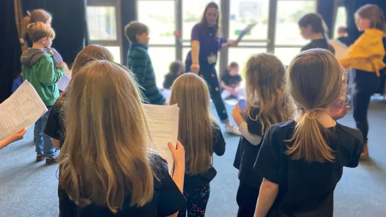 Group of children holding scripts during a theatre workshop or rehearsal session indoors.