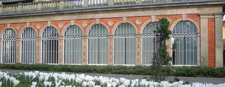 A row of ornate Victorian glass-houses with red brick arches and white metal frames, with flowering plants in the foreground.