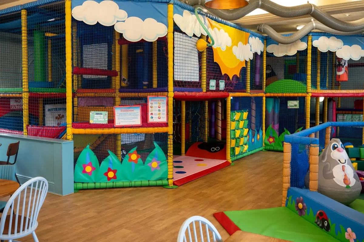 Colourful indoor play area with large soft-play structures, netting, climbing frames and themed decorations for young children.