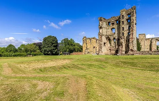 Ruined stone castle with tower standing in open grassland under blue sky.