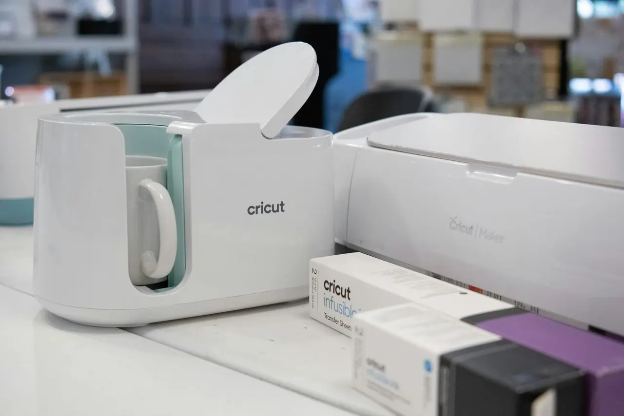 Cricut cutting machine and supplies on a craft workshop table.