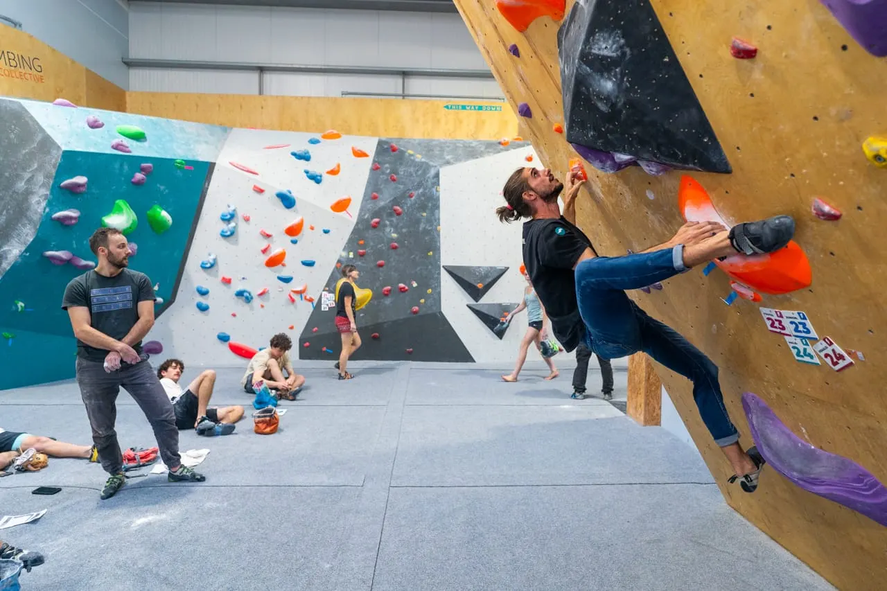 Indoor rock climbing wall with multiple climbers of various ages ascending wooden and painted walls with coloured holds.