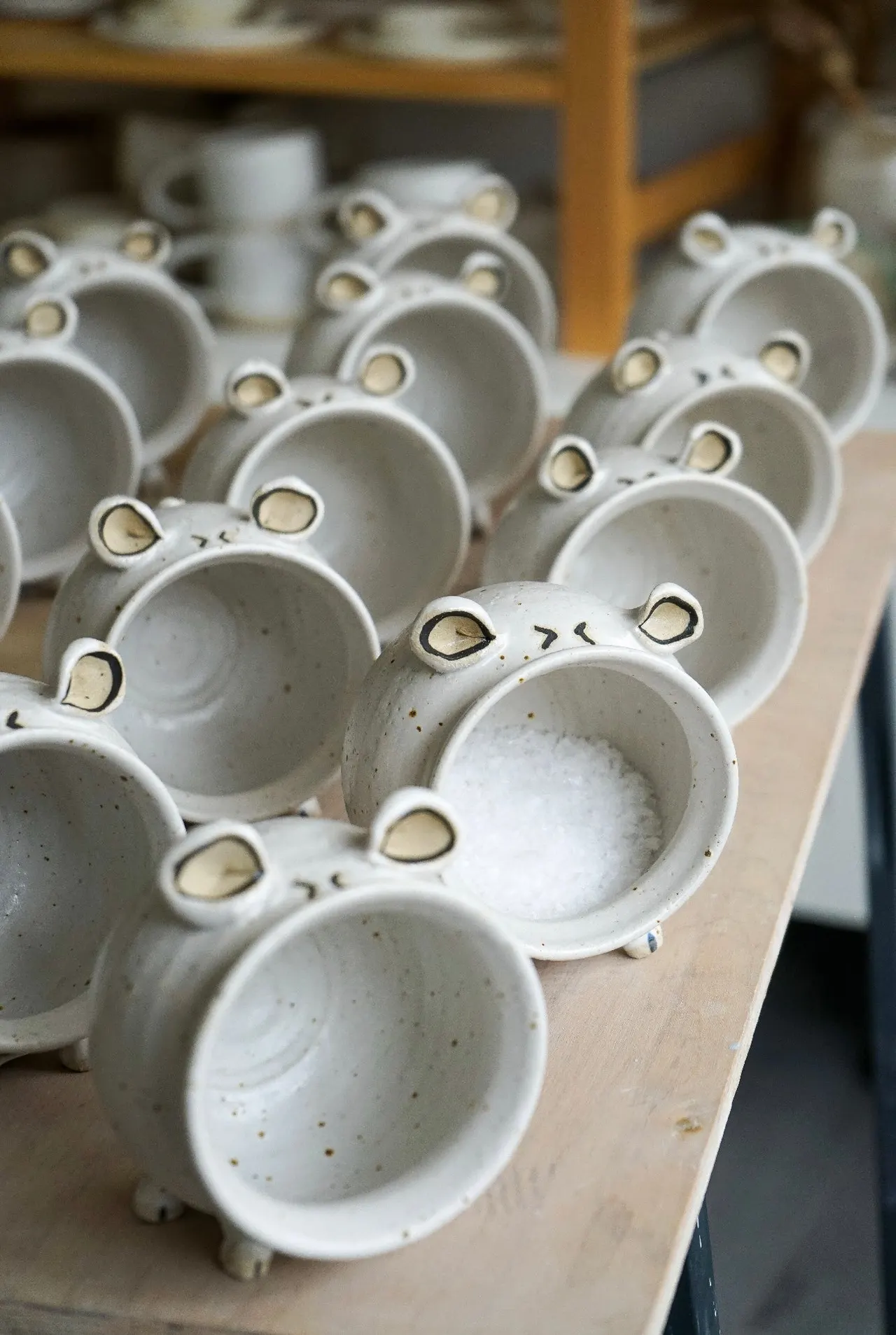 Multiple handmade ceramic bowls shaped like animal faces with ears and features, arranged in rows on a wooden surface.