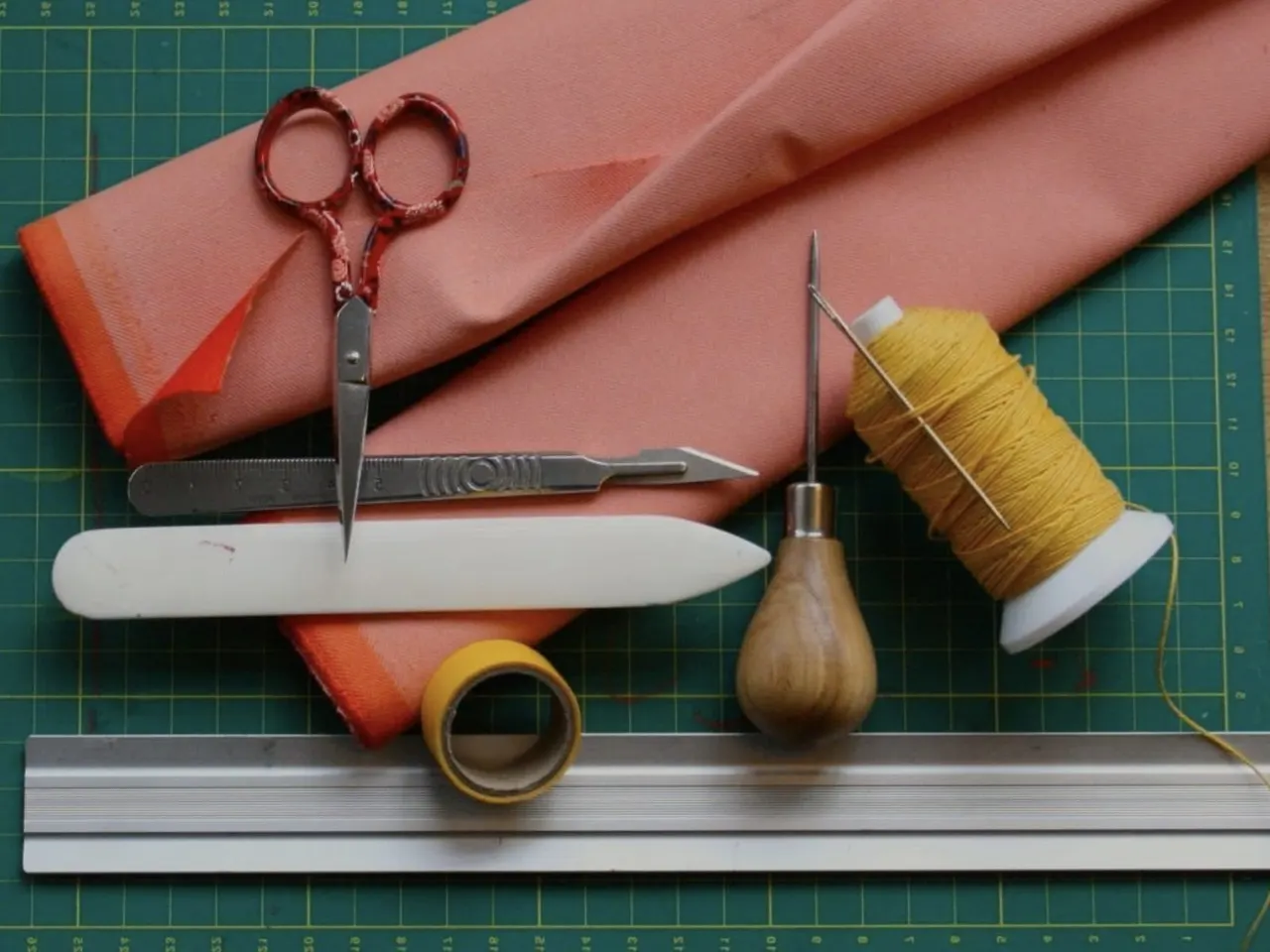 Craft tools including scissors, needle, thread and fabric arranged on a cutting mat.